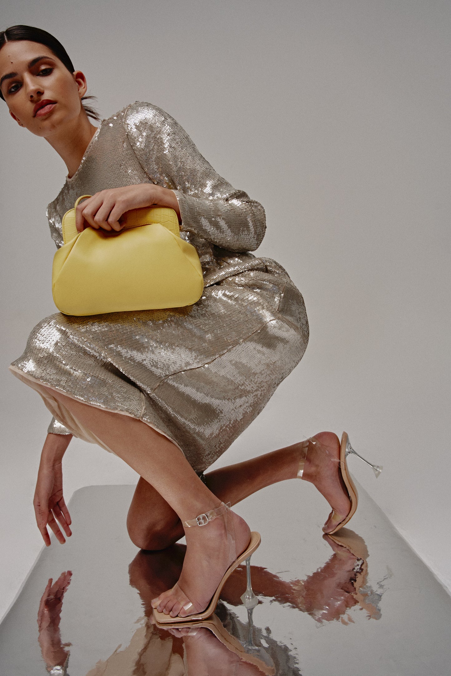 Chica vestida de fiesta agachada con un bolso amarillo