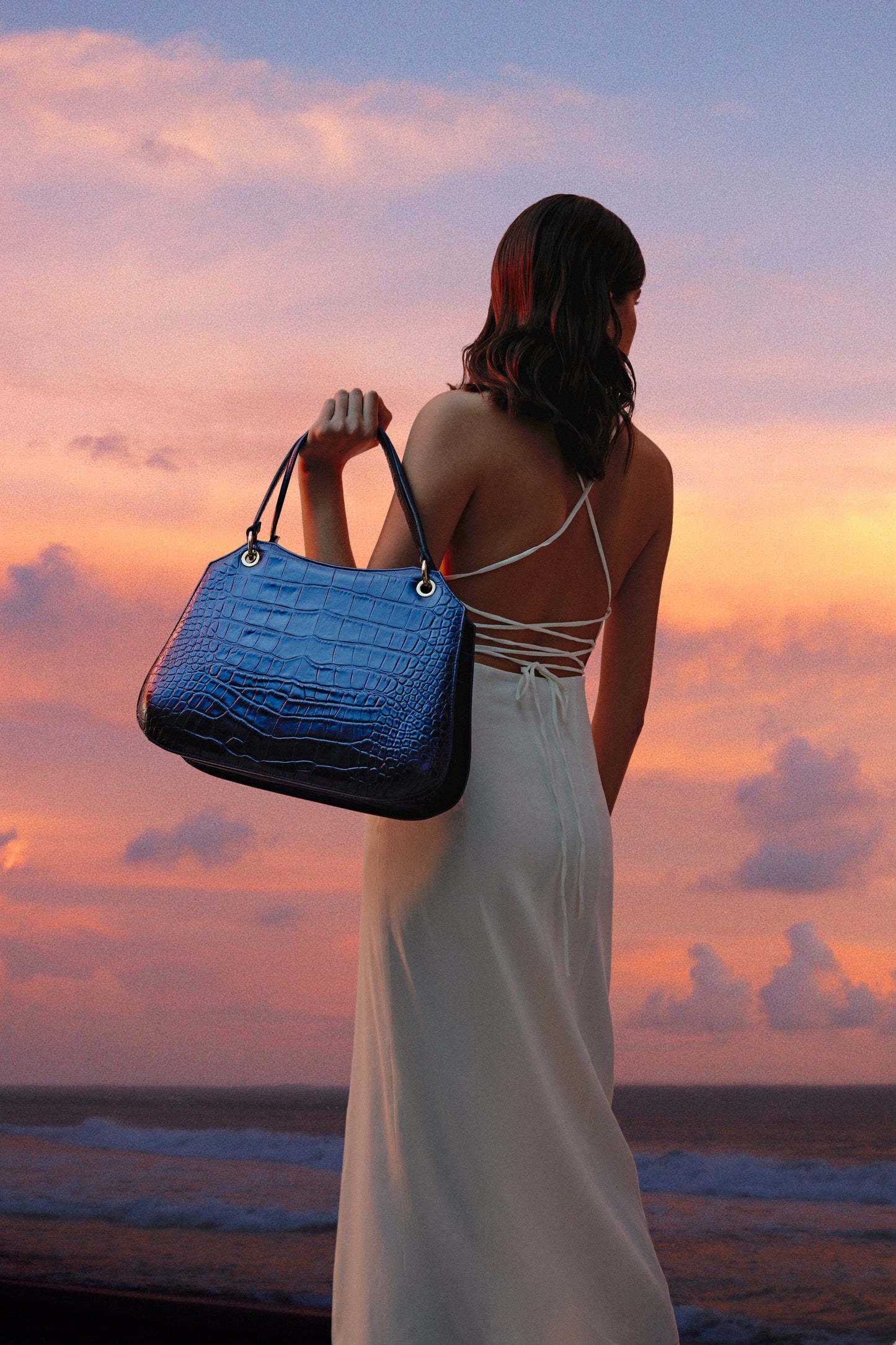 Mujer con vestido blanco de espaldas con bolso azul marino de mano
