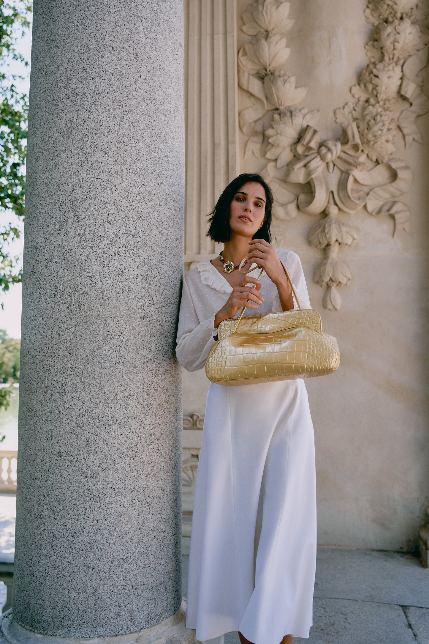 Chica posando junto a su nuevo bolso de hombro metalizado color oro