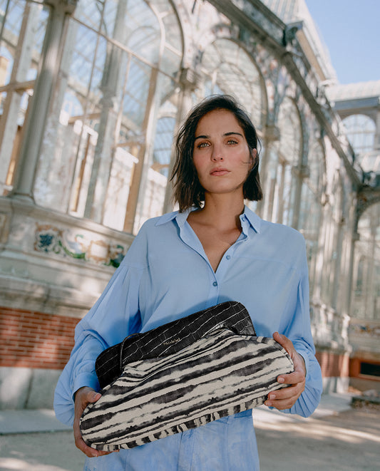 Mujer de azul posando con un bolso negro cebra