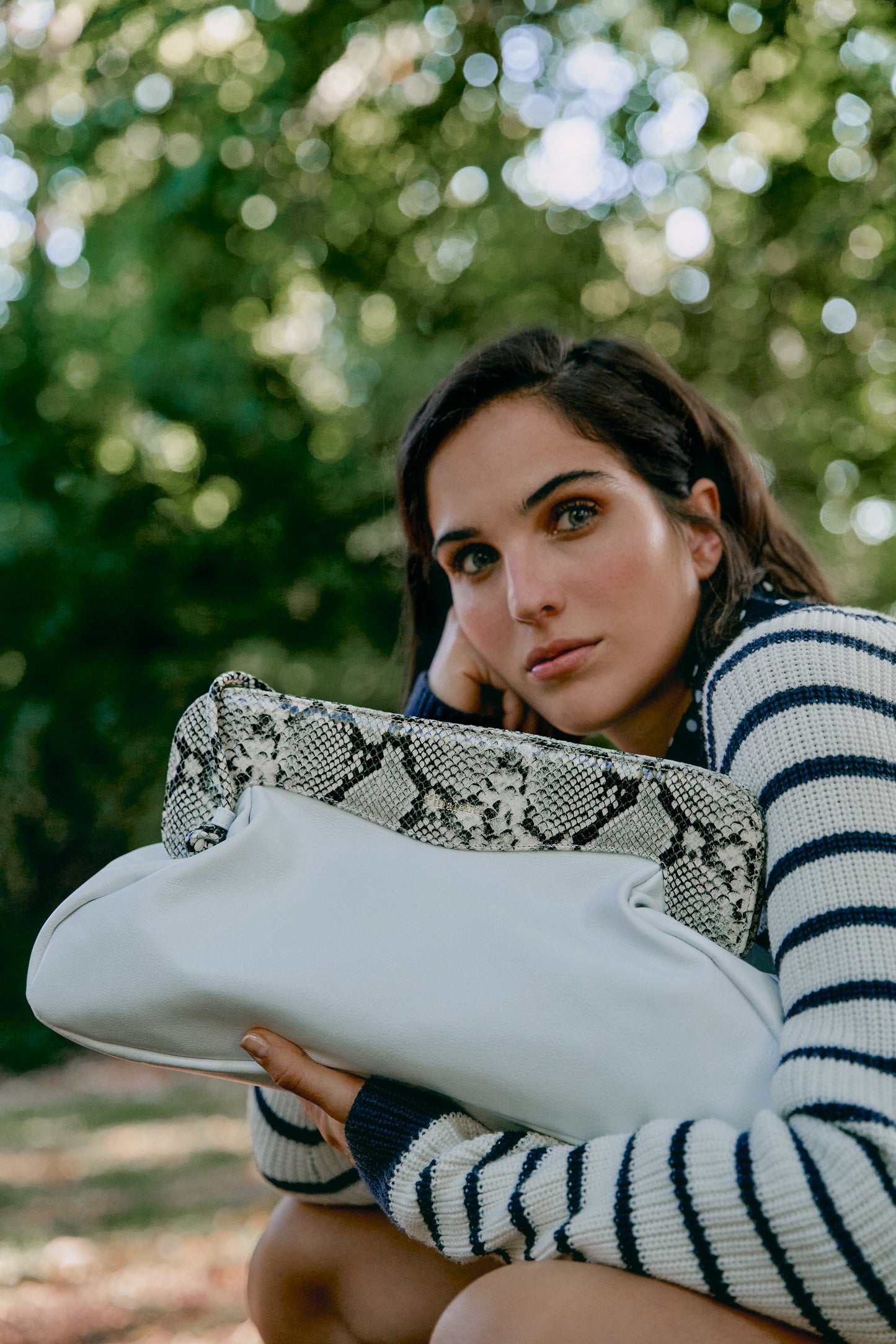 Mujer agachada sosteniendo un bolso blanco color blanco con la solapa con efecto piel de serpiente