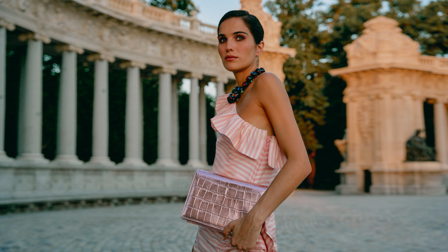 Chica posando con un bolso de fiesta rosa metalizado efeto piel de cocodrilo