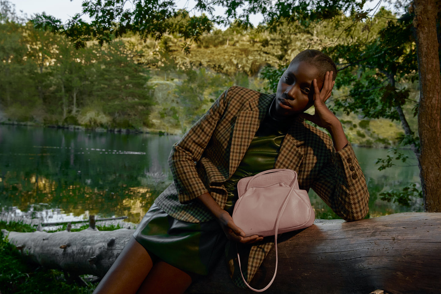 Chica negra posando junto a un río con un bolso rosa claro