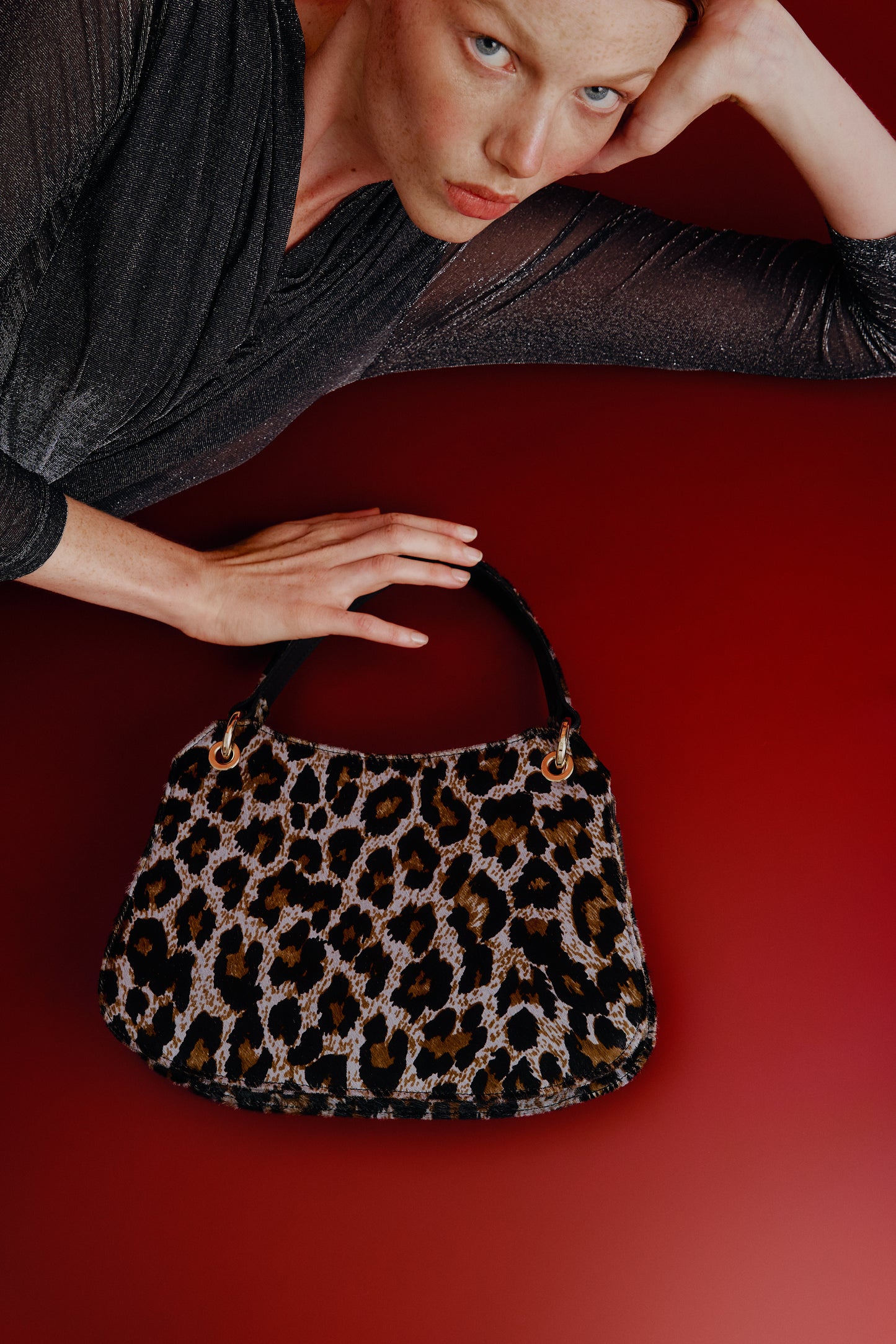 Mujer tumbada posando junto a un bolso de mano con estampado de leopardo gris