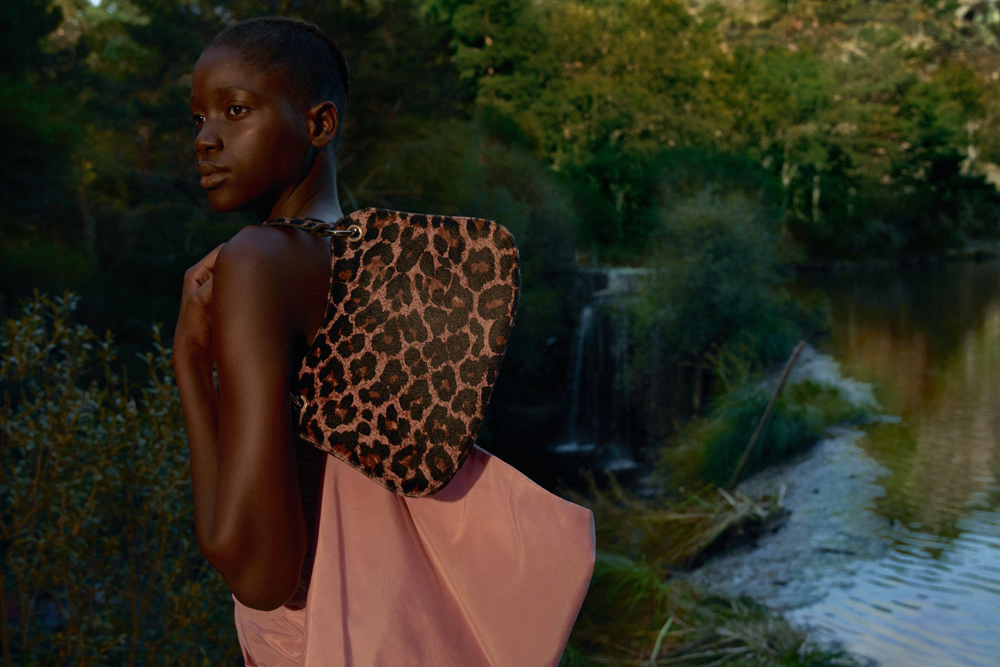Chica negra posando junto a un río con un Bolso estampado leopardo rosa