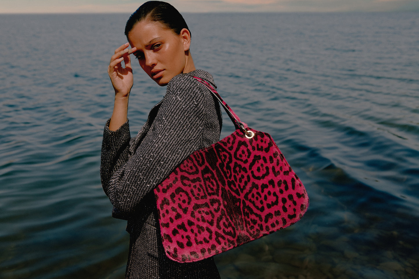 Mujer junto al mar posando con un bolso de leopardo color fucsia