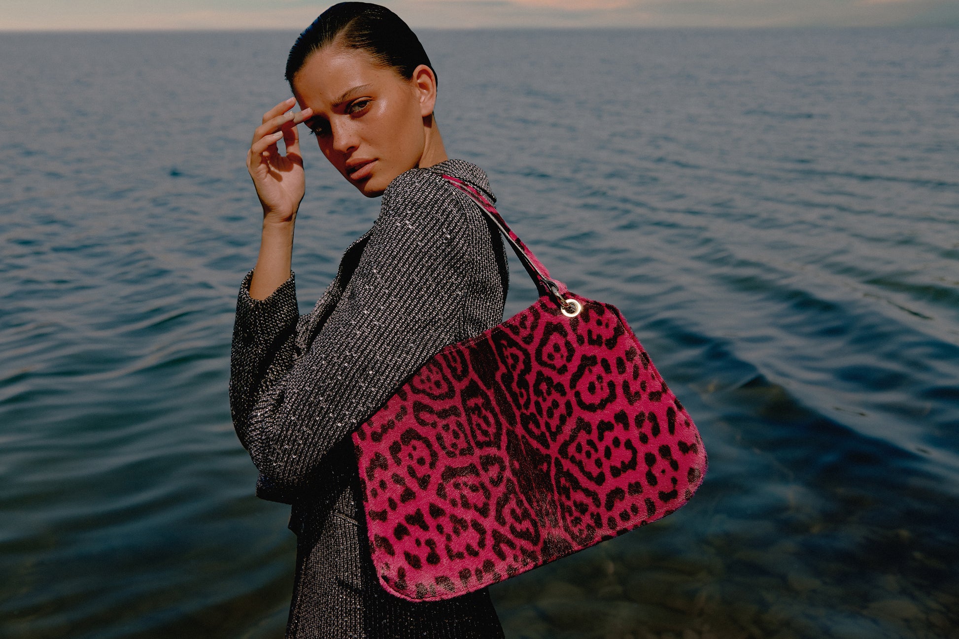 Mujer junto al mar posando con un bolso de leopardo color fucsia