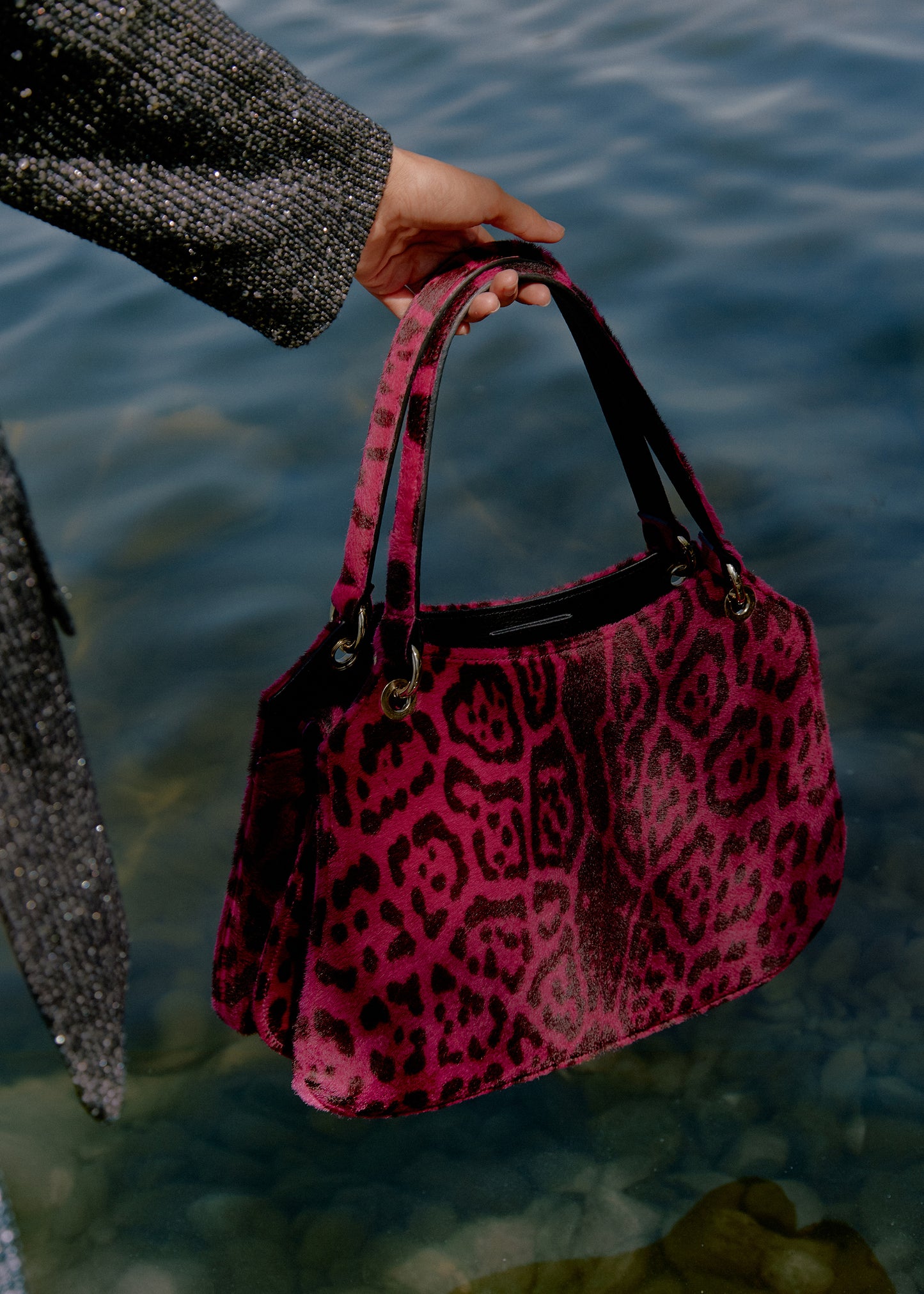 Mujer agarrando las asas de un bolso con estampado de leopardo fucsia junto al mar
