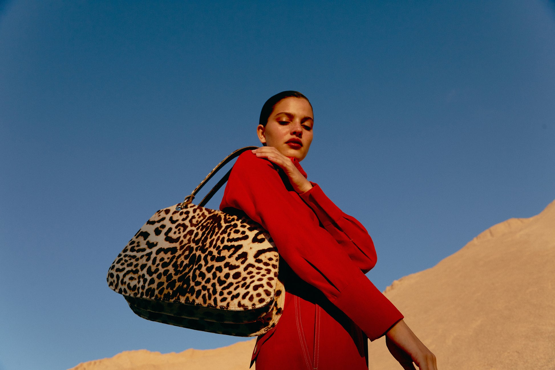 Mujer de rojo posando con un bolso de leopardo natural al hombro