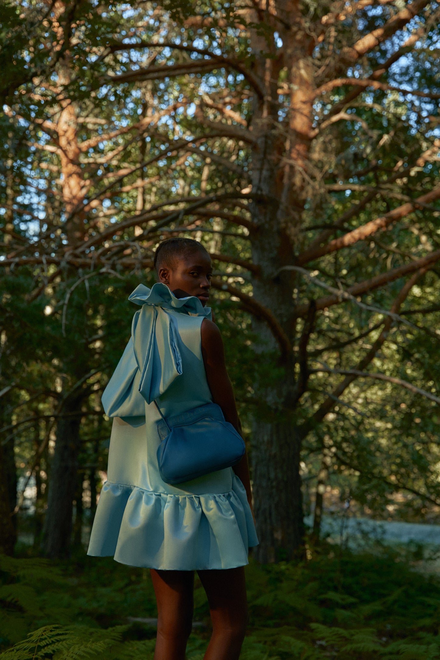 Chica de espaldas posando en un bosque con un bolso de hombro azul