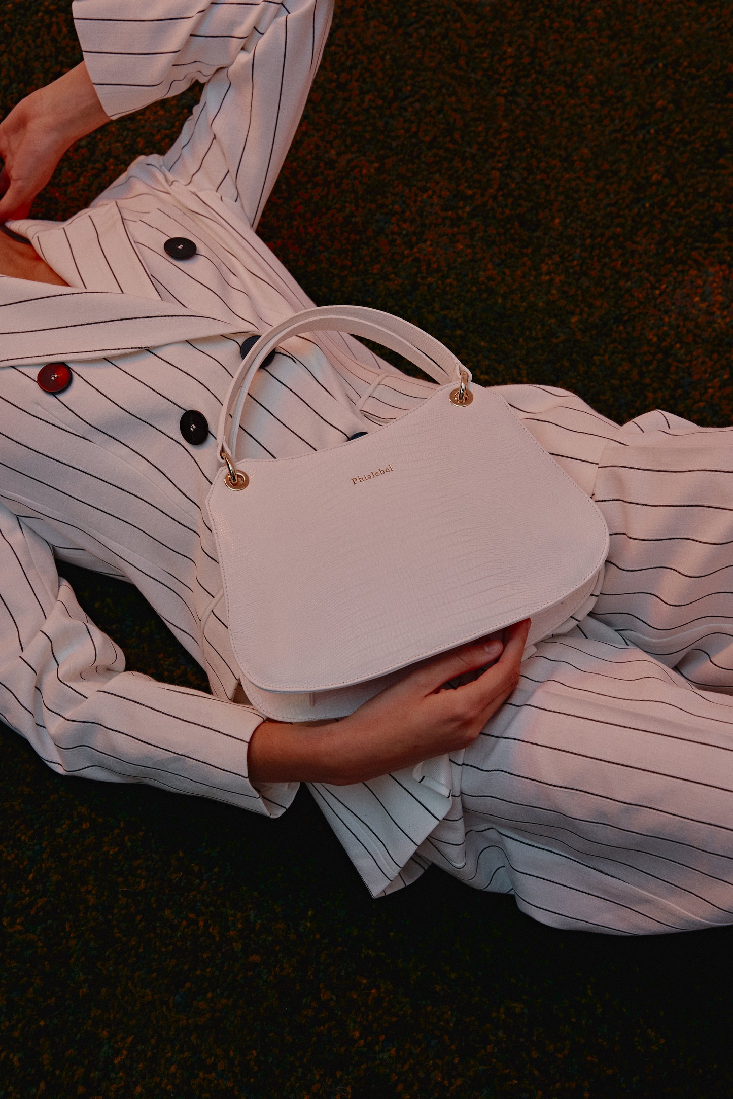 Mujer de blanco tumbada con un bolso blanco metalizado efecto lizard